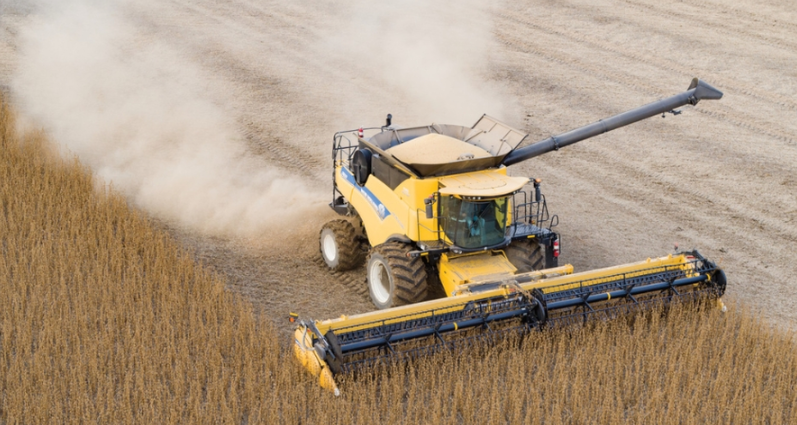 A 2024 New Holland CR Series Twin-Rotor combine in a field, with dust rising around it and trees visible in the background.