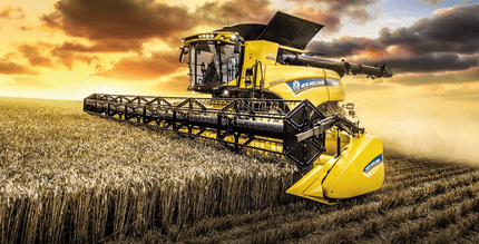 A yellow 2024 New Golland CR Series Twin-Rotor combine harvesting a field at sunset.