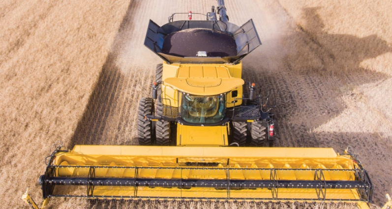 A 2024 New Holland CR11 combine in a field, with dust trailing around it.