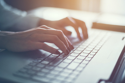 Close-up of a woman's hands typing at a laptop keyboard.