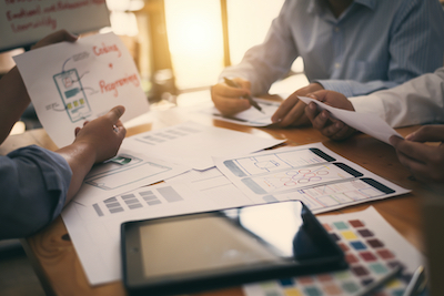 Close-up of a development team examining their designs on a wooden table. 