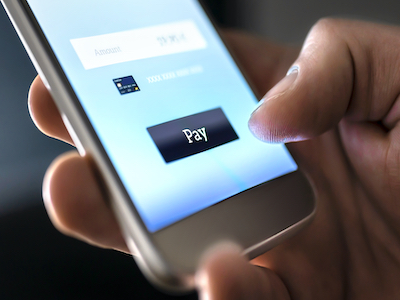 Close-up of a smartphone screen that shows a Pay button, while a man's thumb moves to press the button.