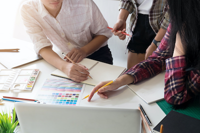 Close-up of three graphic designers, with notebooks and color swatches fanned out on a white table.